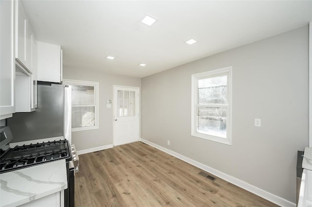 kitchen featuring light hardwood / wood-style flooring, white cabinetry, light stone counters, and appliances with stainless steel finishes