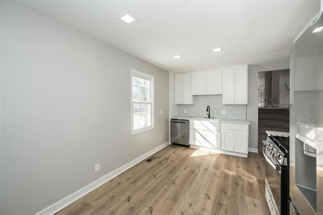 kitchen featuring stainless steel appliances, decorative backsplash, white cabinets, light hardwood / wood-style flooring, and sink