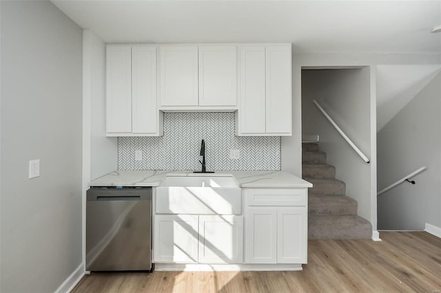 kitchen with light stone countertops, stainless steel dishwasher, white cabinets, and sink