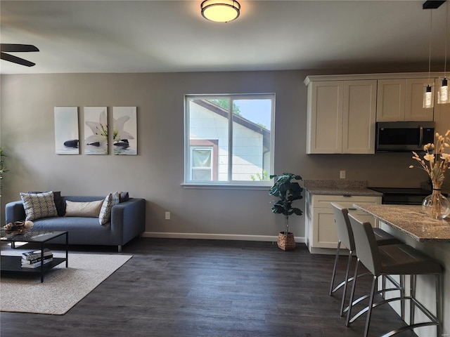 kitchen featuring white cabinets, dark stone countertops, a breakfast bar area, dark hardwood / wood-style flooring, and pendant lighting