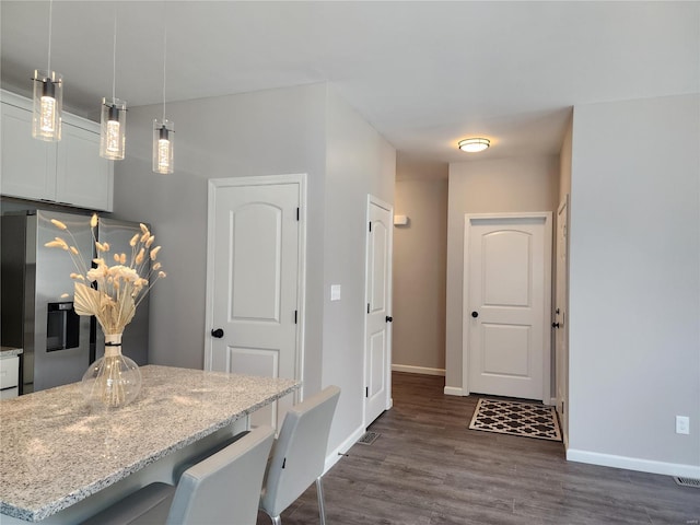 kitchen featuring white cabinets, a breakfast bar area, light stone countertops, pendant lighting, and stainless steel fridge