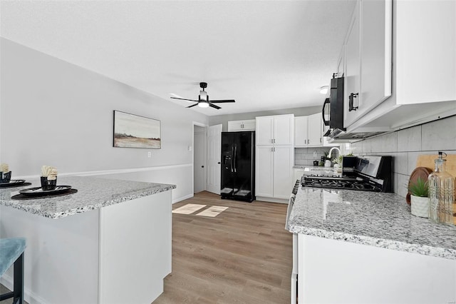 kitchen with black appliances, kitchen peninsula, white cabinetry, light stone countertops, and a breakfast bar area