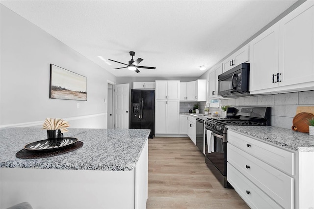 kitchen featuring decorative backsplash, light stone countertops, white cabinetry, and black appliances