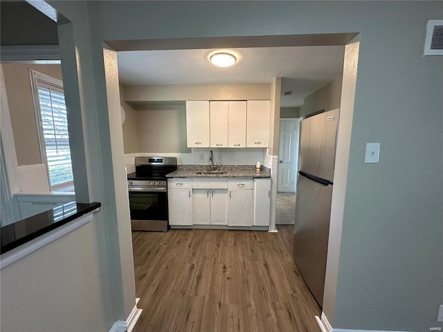 kitchen featuring light stone countertops, appliances with stainless steel finishes, white cabinetry, light hardwood / wood-style floors, and sink