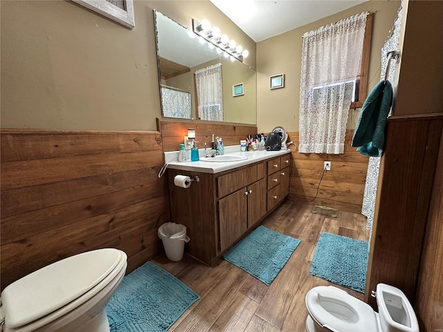 bathroom with toilet, vanity, wood walls, and hardwood / wood-style flooring