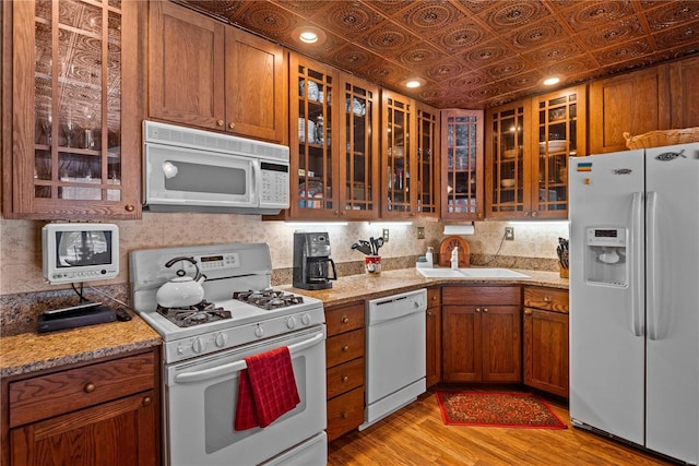 kitchen featuring light wood-type flooring, light stone countertops, sink, and white appliances