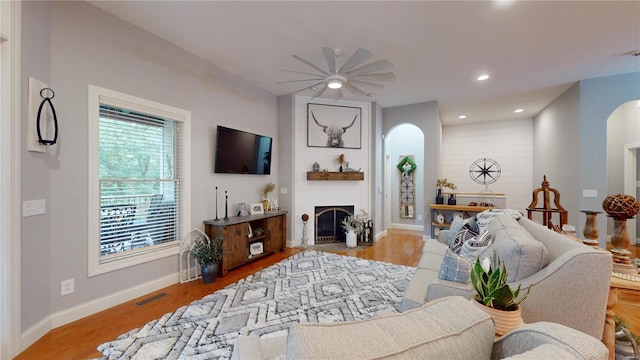 living room featuring ceiling fan, light wood-type flooring, and a fireplace