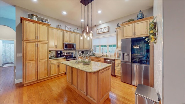 kitchen featuring appliances with stainless steel finishes, decorative light fixtures, an island with sink, sink, and light stone counters