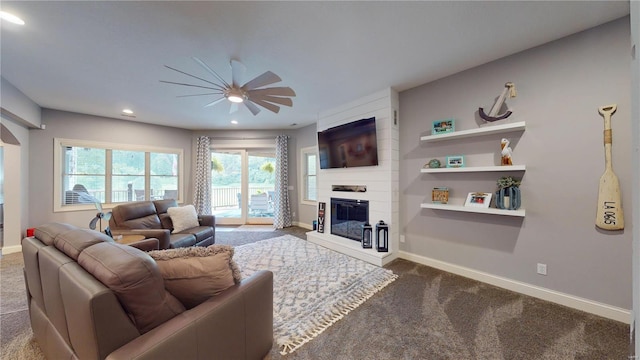 carpeted living room featuring ceiling fan and a large fireplace