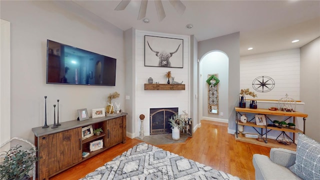 living room featuring ceiling fan, light wood-type flooring, and a large fireplace