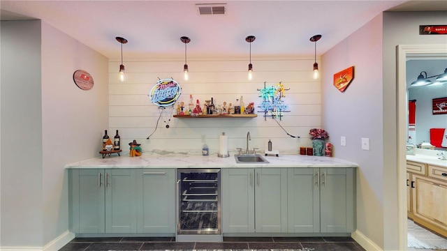 bar featuring decorative light fixtures, sink, beverage cooler, and light stone counters