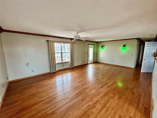 unfurnished living room with ornamental molding, a textured ceiling, baseboards, and wood finished floors