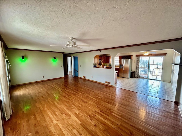 unfurnished living room with light wood-type flooring, crown molding, arched walkways, and ceiling fan