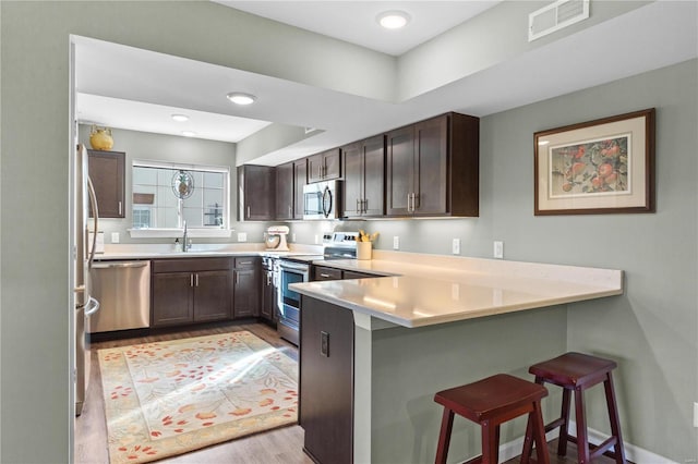 kitchen with stainless steel appliances, sink, kitchen peninsula, light hardwood / wood-style flooring, and a breakfast bar area