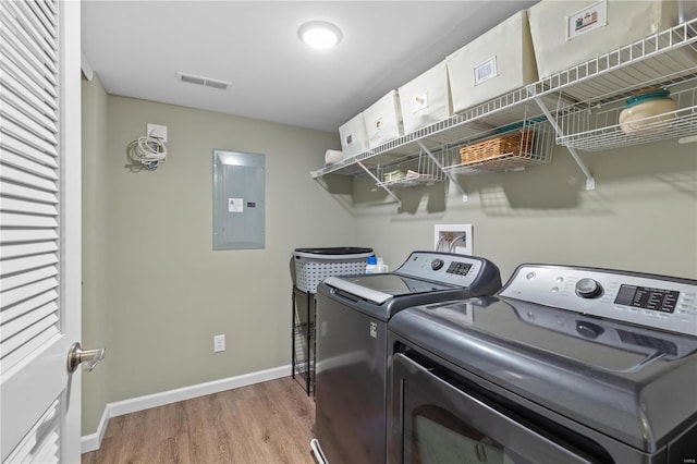 laundry room with electric panel, light hardwood / wood-style flooring, and washing machine and clothes dryer