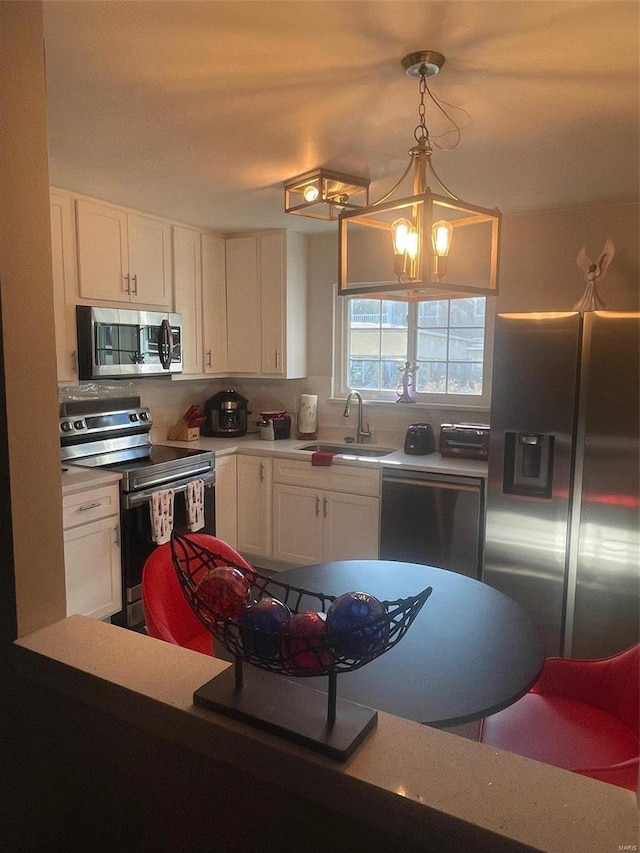 kitchen with appliances with stainless steel finishes, white cabinetry, hanging light fixtures, and sink