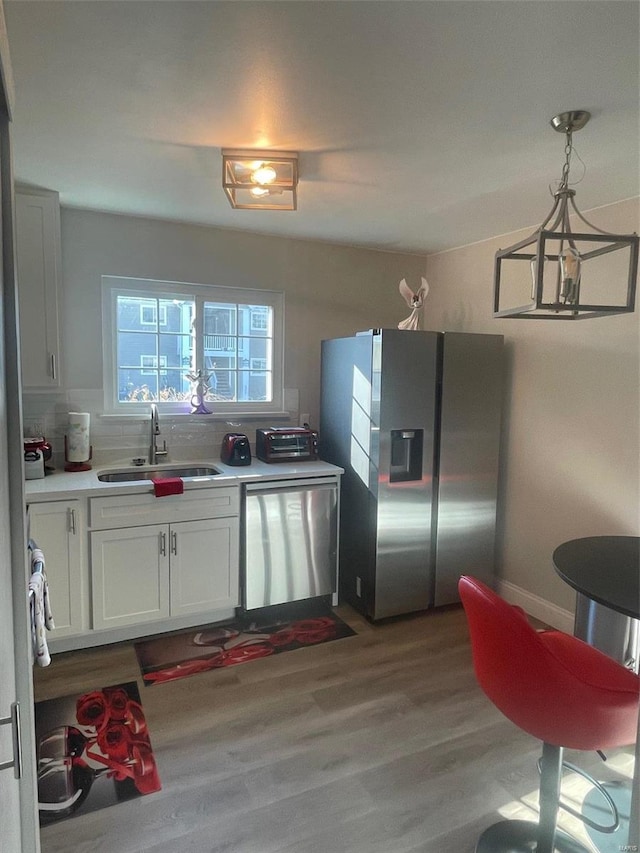 kitchen featuring appliances with stainless steel finishes, decorative light fixtures, white cabinetry, sink, and light wood-type flooring