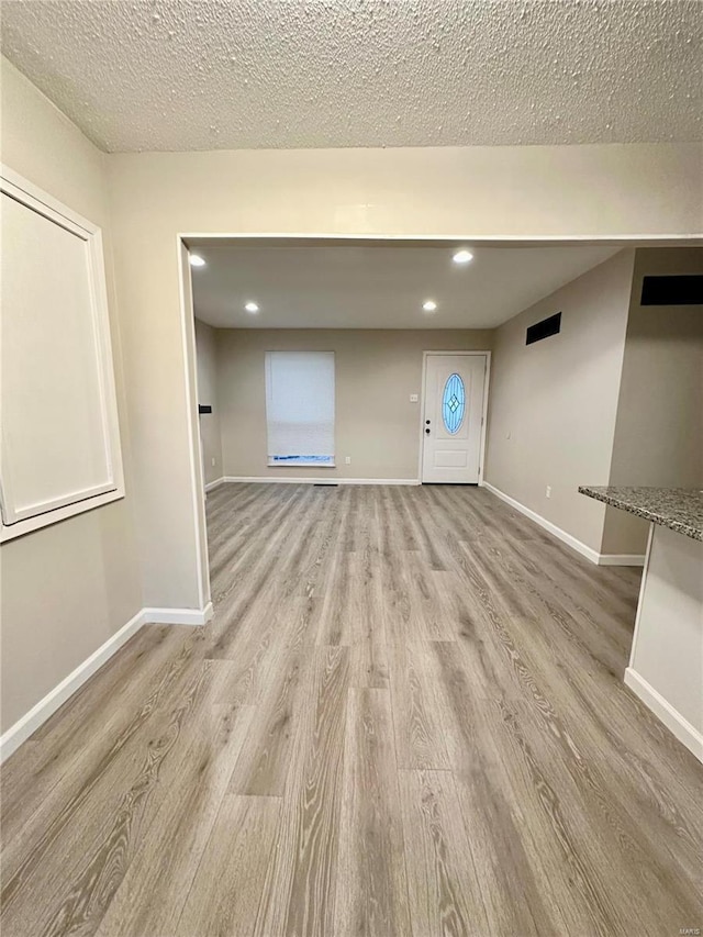 unfurnished living room with a textured ceiling and light hardwood / wood-style floors