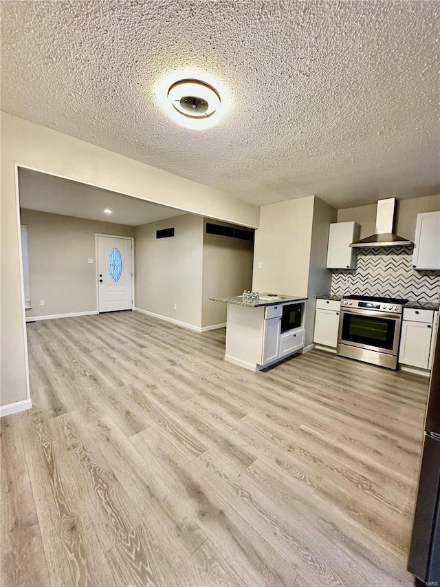 kitchen featuring white cabinetry, stainless steel range oven, built in microwave, wall chimney exhaust hood, and light wood-type flooring