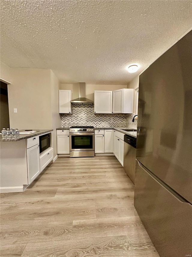 kitchen with white cabinets, wall chimney exhaust hood, light hardwood / wood-style floors, and black appliances