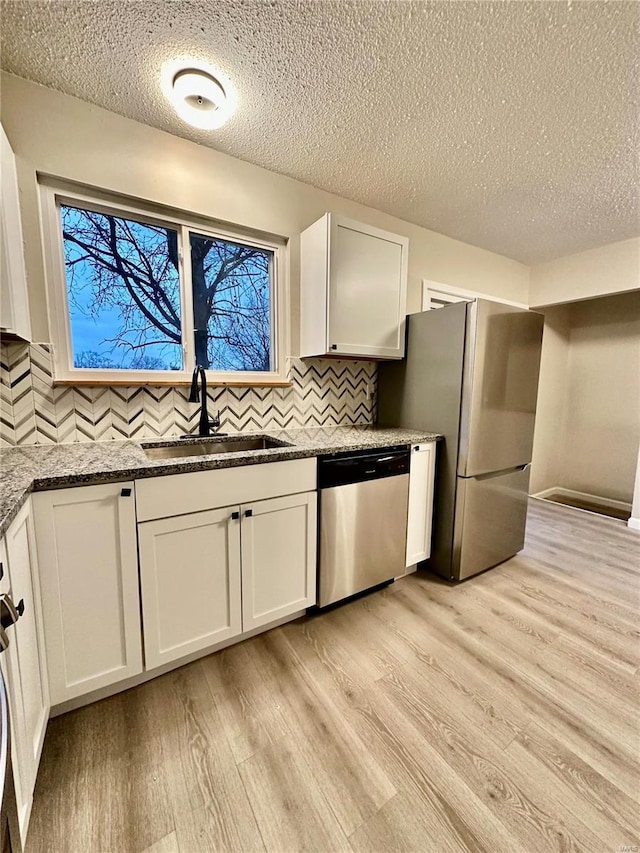 kitchen with sink, white cabinetry, stone counters, stainless steel appliances, and light hardwood / wood-style floors