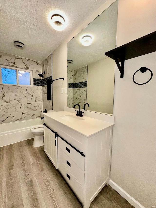 full bathroom featuring tiled shower / bath, hardwood / wood-style floors, vanity, toilet, and a textured ceiling