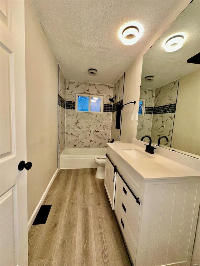 bathroom featuring hardwood / wood-style floors, vanity, tiled shower, toilet, and a textured ceiling