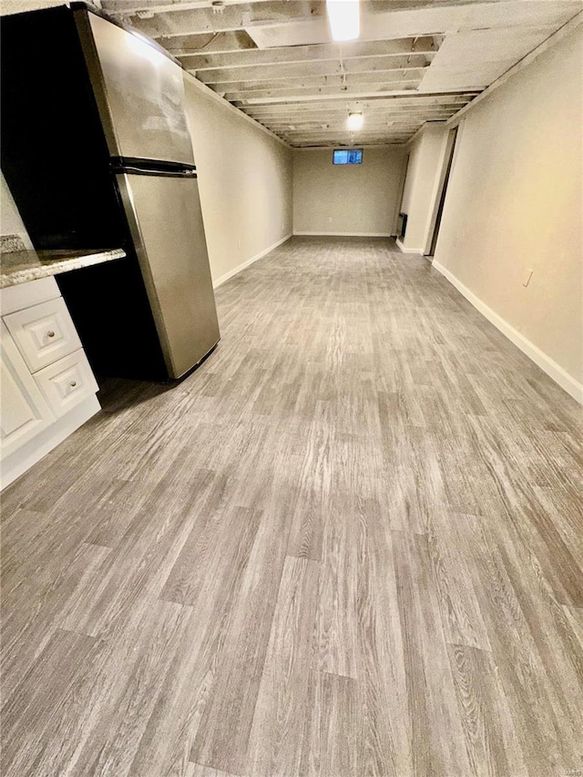 basement with light hardwood / wood-style flooring and stainless steel refrigerator