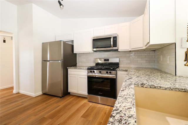 kitchen with white cabinetry, appliances with stainless steel finishes, tasteful backsplash, vaulted ceiling, and light hardwood / wood-style flooring