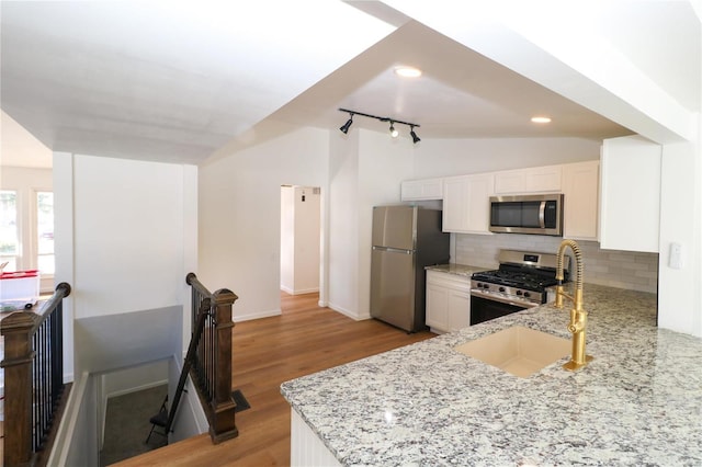 kitchen with appliances with stainless steel finishes, lofted ceiling, white cabinets, and light stone counters