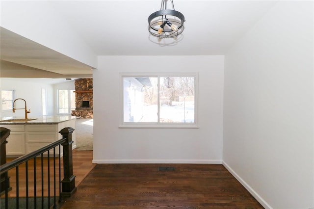 dining area featuring dark hardwood / wood-style floors, sink, a stone fireplace, and a chandelier