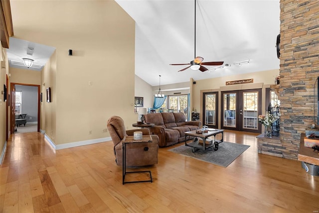 living room featuring high vaulted ceiling, track lighting, light hardwood / wood-style floors, ceiling fan with notable chandelier, and french doors