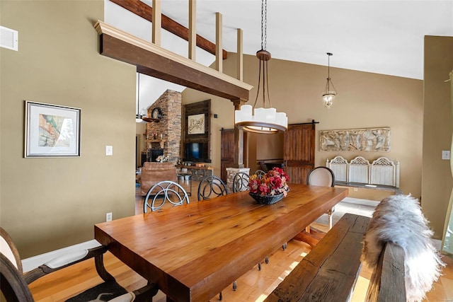 dining space featuring a towering ceiling, a stone fireplace, and light hardwood / wood-style floors