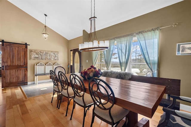 dining room featuring a barn door, high vaulted ceiling, and light wood-type flooring