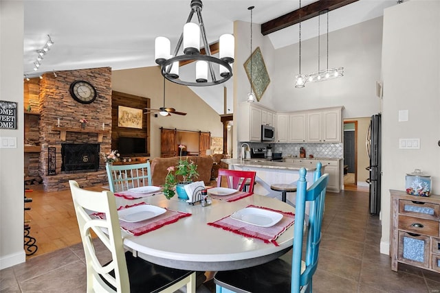 dining room with a stone fireplace, sink, dark tile patterned floors, ceiling fan, and beam ceiling