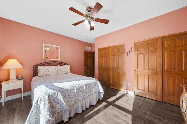 bedroom with ceiling fan, two closets, and dark hardwood / wood-style flooring