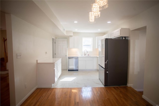 kitchen featuring decorative light fixtures, black fridge, stainless steel dishwasher, white cabinets, and sink