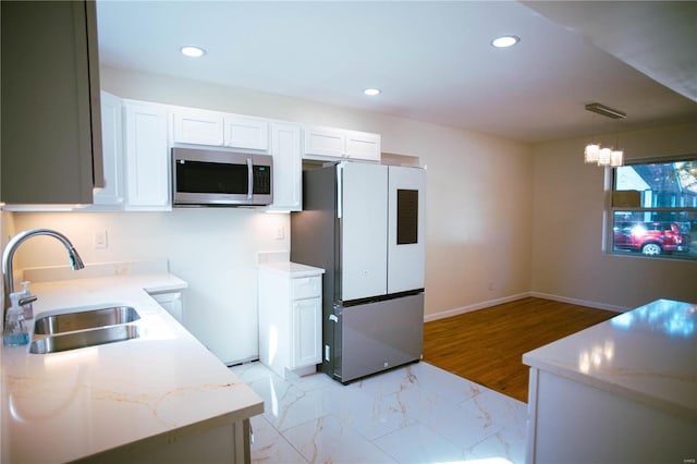 kitchen with an inviting chandelier, appliances with stainless steel finishes, pendant lighting, white cabinets, and sink