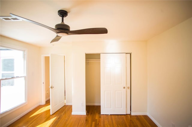 unfurnished bedroom with ceiling fan, a closet, wood-type flooring, and multiple windows