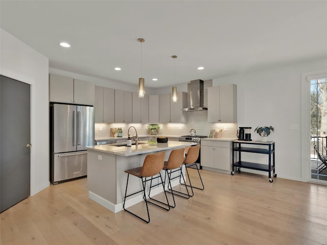 kitchen featuring stainless steel appliances, a sink, a kitchen breakfast bar, light countertops, and wall chimney range hood