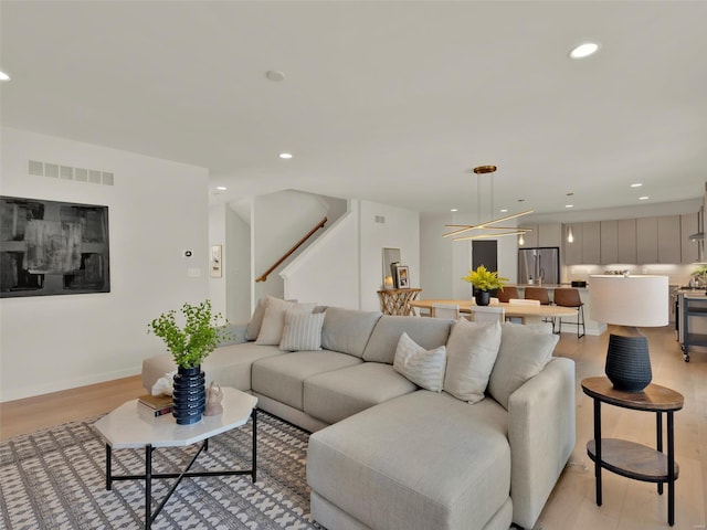 living area with recessed lighting, visible vents, baseboards, stairway, and light wood finished floors