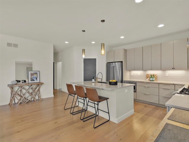 kitchen featuring high end fridge, hanging light fixtures, light countertops, modern cabinets, and a center island with sink