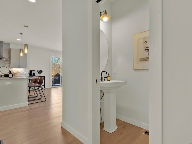 bathroom with baseboards, backsplash, wood finished floors, a sink, and recessed lighting