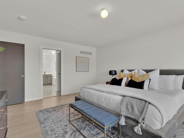 bedroom with light wood-style floors, visible vents, ensuite bath, and baseboards