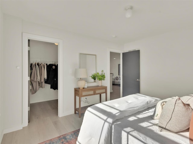 bedroom with a walk in closet, a closet, baseboards, and light wood finished floors