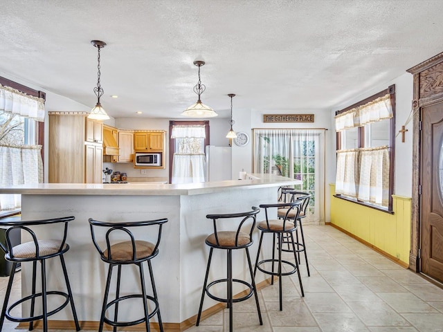 kitchen with a kitchen bar, hanging light fixtures, a textured ceiling, white fridge, and a large island