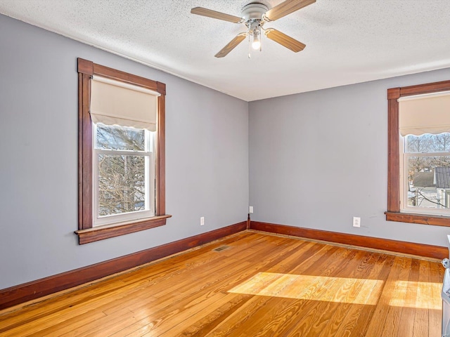 empty room featuring light wood-type flooring, visible vents, baseboards, and a textured ceiling