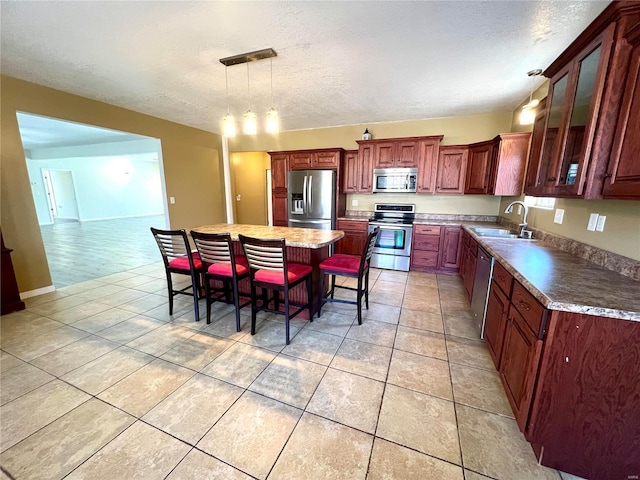 kitchen featuring a breakfast bar area, appliances with stainless steel finishes, light tile patterned flooring, a kitchen island, and sink