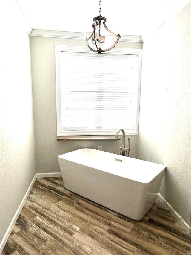 bathroom with crown molding, a bath, an inviting chandelier, and hardwood / wood-style flooring