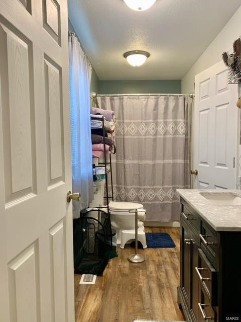 full bath featuring toilet, a shower with curtain, wood finished floors, and vanity